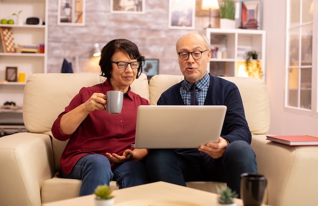 Vieux Couple De Personnes âgées Utilisant Un Ordinateur Portable Moderne Pour Discuter Avec Leur Petit-fils. Grand-mère Et Grand-père Utilisant La Technologie Moderne