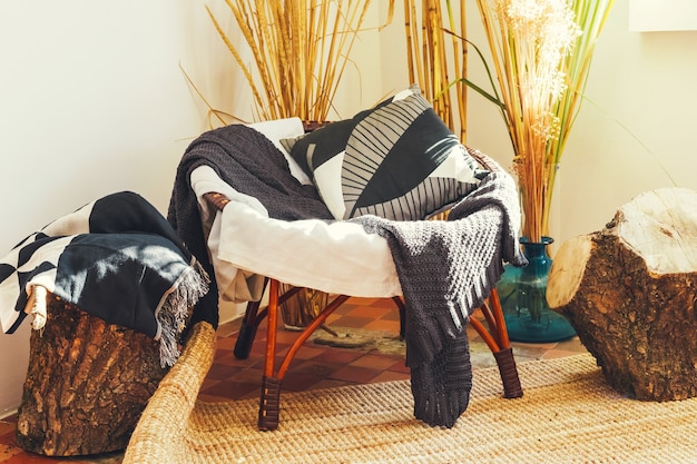 Vieux fauteuil confortable avec plaid et coussin contre des vases avec des branches de plantes sèches