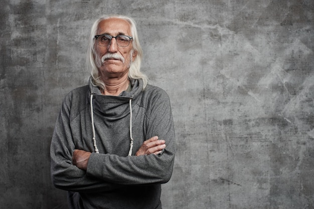 Un vieux grand-père cool aux cheveux gris de race blanche avec des lunettes regarde avec incrédulité la caméra avec les bras croisés et le visage sérieux avec un espace de copie en studio