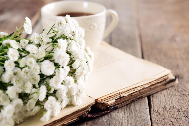 Vieux livre avec de belles fleurs et une tasse de thé sur une table en bois se bouchent