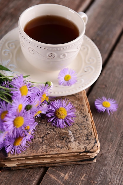 Vieux livre avec de belles fleurs et une tasse de thé sur une table en bois se bouchent