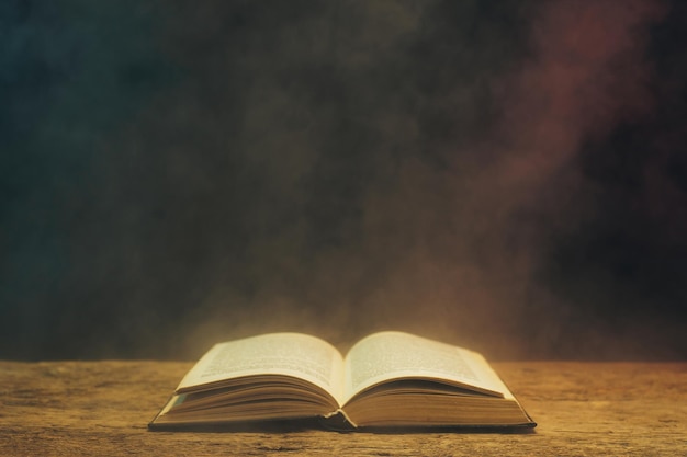 Un vieux livre sur une table en bois de chêne sur fond de fumée bleue et rouge