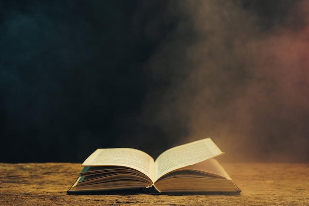 Un vieux livre sur une table en bois de chêne sur fond de fumée bleue et rouge