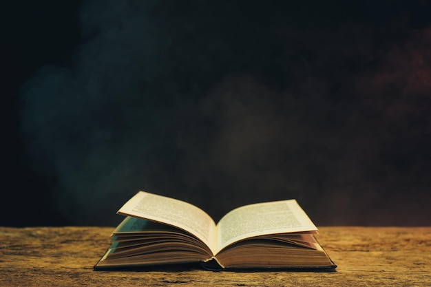 Un vieux livre sur une table en bois de chêne sur fond de fumée bleue et rouge