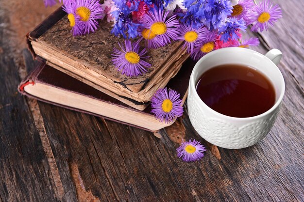 Vieux livres avec de belles fleurs et une tasse de thé sur une table en bois se bouchent