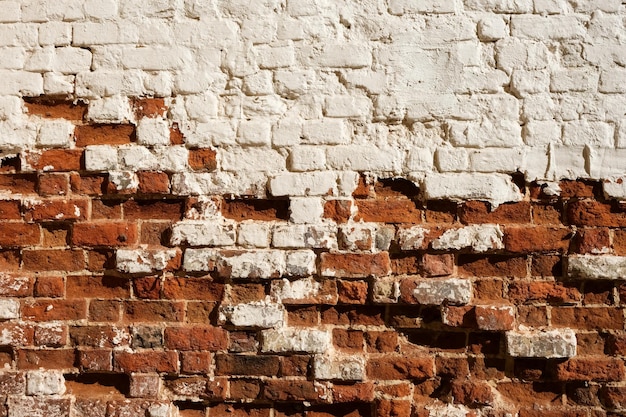 Vieux mur de briques peintes avec des éléments en ruine. Surface texturée inégale.