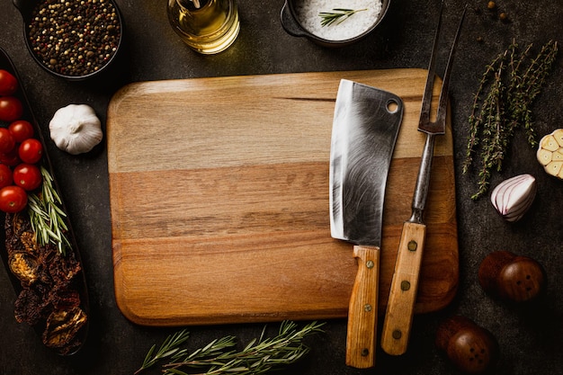 Vieux outils de cuisine de boucher sur une planche à découper en béton foncé avec des épices, du sel et du poivre à plat