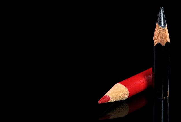 Vieux petits crayons d'ardoise en bois rouges et noirs aiguisés sur fond noir en miroir, espace pour le texte sur la gauche