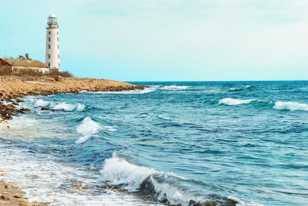 Vieux phare sur la côte de la mer. Tempête, vagues et ciel bleu.