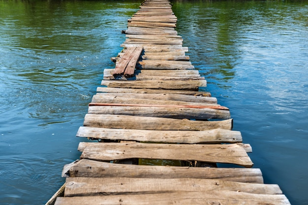 Vieux pont en bois à travers la rivière avec des arbres verts sur les rives