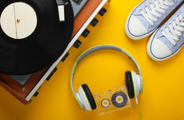 Vieux tourne-disque vinyle avec casque stéréo, cassette audio et baskets sur surface jaune