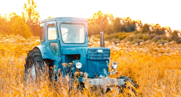 Vieux tracteur bleu sur le terrain d'herbes hautes