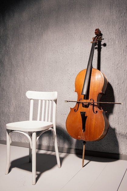 Vieux violoncelle battu et chaise debout près d'un mur texturé gris à l'école ou salle de pratique.