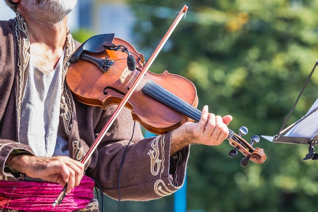 Un vieux violoniste dans un vieux costume exécute une pièce musicale en plein air_