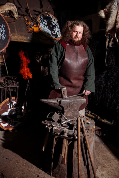 Photo viking forge des armes et des épées dans la forge. un homme en habit de guerrier est dans la forge.