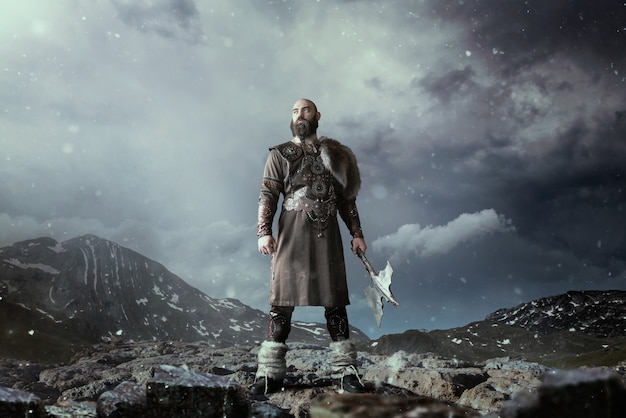 Viking avec hache vêtu de vêtements nordiques traditionnels debout dans les montagnes rocheuses. Ancien guerrier scandinave
