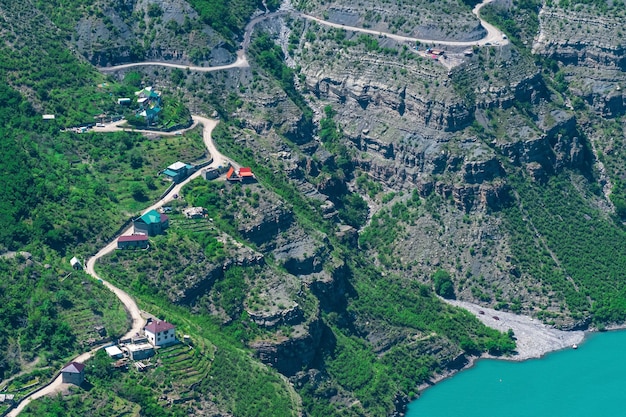 Village de montagne avec jardins potagers en terrasses et une route sur le versant d'une gorge au bord d'une rivière aux eaux bleues