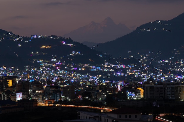 Une ville est éclairée la nuit avec une montagne en arrière-plan.