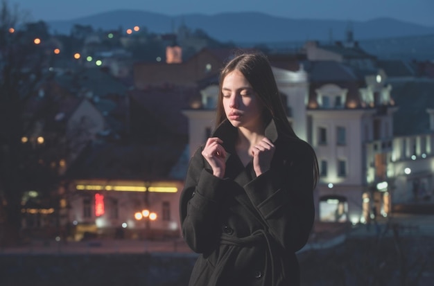 Ville de nuit avec fille, jeune mannequin brune en manteau noir