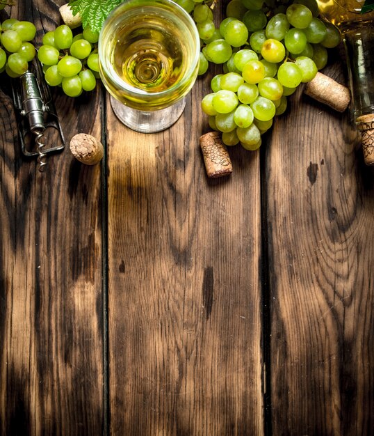 Vin blanc avec des branches de raisin blanc sur table en bois.