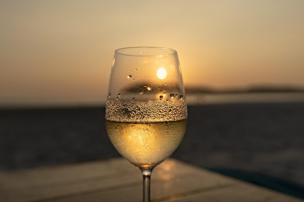 Vin blanc dans le verre embué contre le ciel coucher de soleil sur la plage