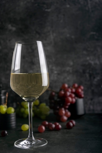 Vin blanc dans un verre à vin avec des raisins rouges et verts sur fond de marbre foncé