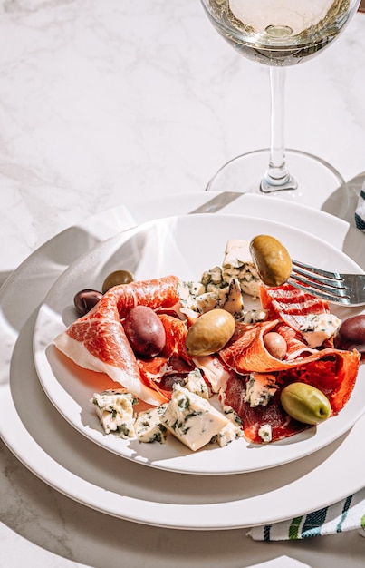 Photo vin blanc frais dans un verre près d'une assiette avec des tranches de jambon et diverses olives une collation légère lors d'une journée chaude cuisine italienne classique