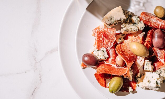 Photo vin blanc frais dans un verre près d'une assiette avec des tranches de jambon et diverses olives une collation légère lors d'une journée chaude cuisine italienne classique