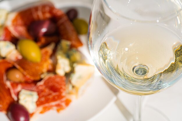 Photo vin blanc frais dans un verre près d'une assiette avec des tranches de jambon, du fromage de colombe et diverses olives