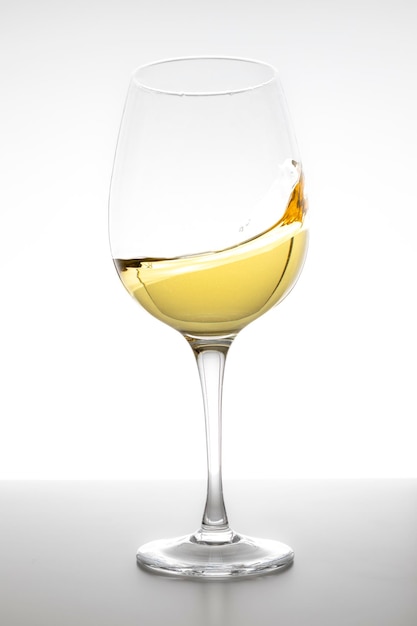 Vin blanc tourbillonnant dans le verre sur fond blanc