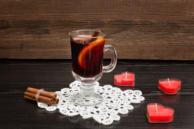 Vin chaud aux épices sur une serviette en dentelle. Bougies en forme de cœur et bâtons de cannelle. Fond en bois