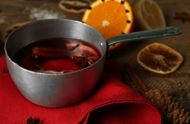 Vin chaud dans une casserole décorée de serviette rouge, cannelle et table en bois orange