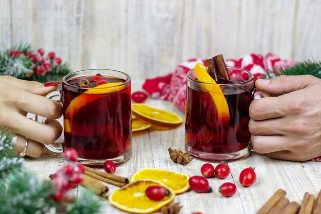 Vin chaud dans les mains des femmes, épices sur table en bois patiné.