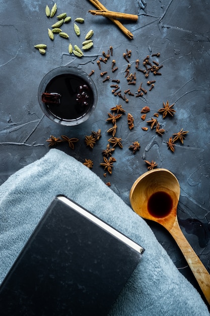 Vin chaud dans une tasse à la main, des épices, une couverture et des livres