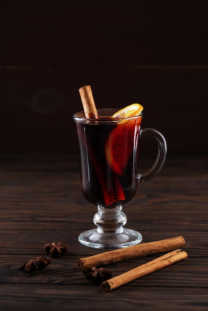 Vin chaud dans un verre à l'orange et aux épices sur fond sombre.