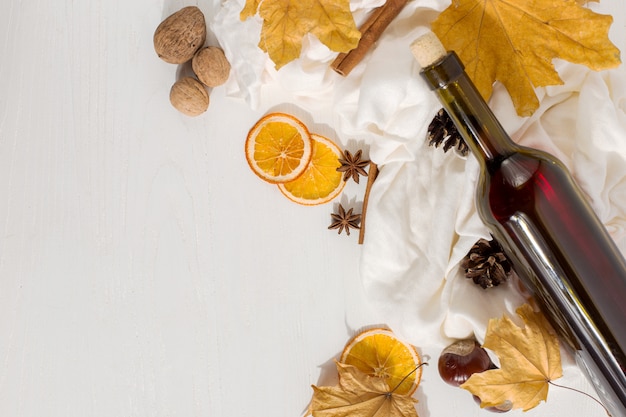 Vin chaud avec des épices, une bouteille, un foulard, des épices, des feuilles sèches et des oranges sur la table. Humeur d'automne, méthode pour garder au chaud dans le froid, fond.