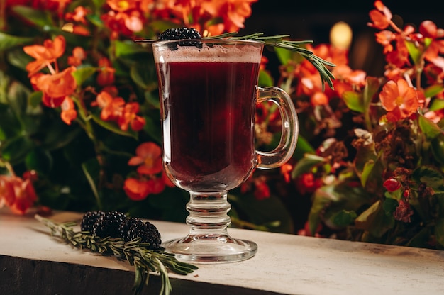 Vin chaud de mûre au romarin dans une tasse en verre sur fond de fleurs