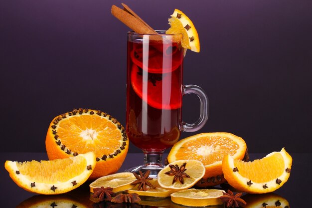 Vin chaud parfumé en verre avec des épices et des oranges autour sur fond violet