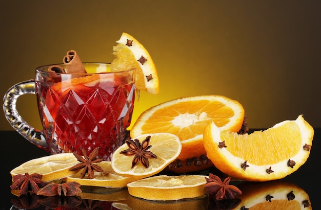 Vin chaud parfumé en verre avec des épices et des oranges autour sur une surface jaune