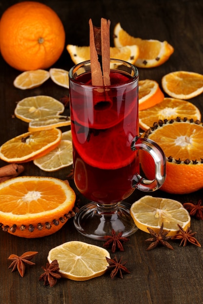 Vin chaud parfumé en verre avec des épices et des oranges autour sur une table en bois