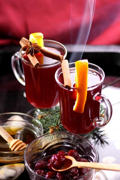 Vin chaud rouge miel d'abeille tranches d'oranges et d'épices sur fond sombre décoration de Noël avec des branches d'épinette et une serviette rouge