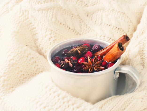 Vin chaud en tasse avec canneberge et épices sur fond de pull blanc