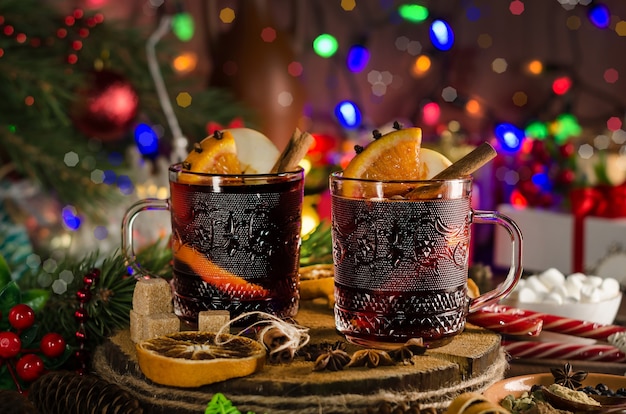 Vin chaud avec tranche d'orange, bâton de cannelle et épices sur fond de guirlandes festives. Style sombre