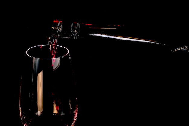 Le vin fortifié rouge est versé dans une photographie d'art de gobelet en verre sur un plan rapproché de fond noir