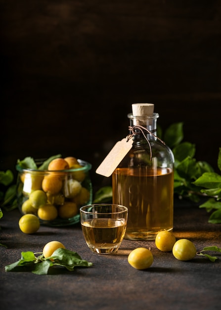 Vin ou liqueur fait maison de prune de cerise jaune dans un petit verre et de fruits mûrs sur une table sombre