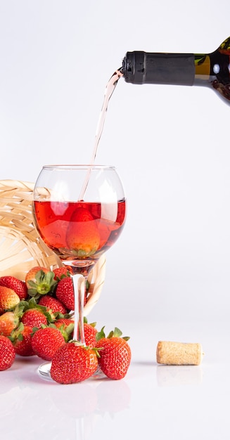 Vin rose servi dans un verre en cristal avec de belles fraises sur une surface blanche, mise au point sélective.