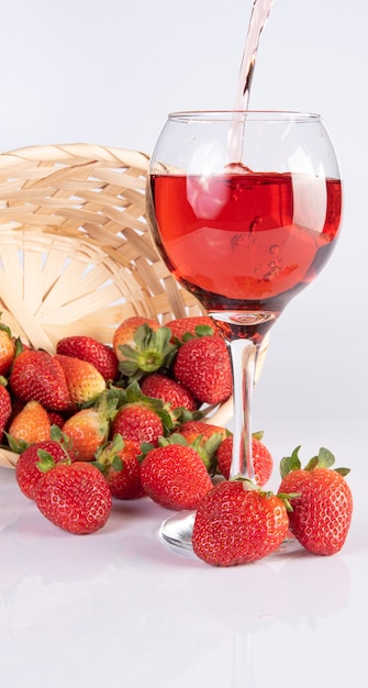 Vin rose servi dans un verre en cristal avec de belles fraises sur une surface blanche, mise au point sélective.