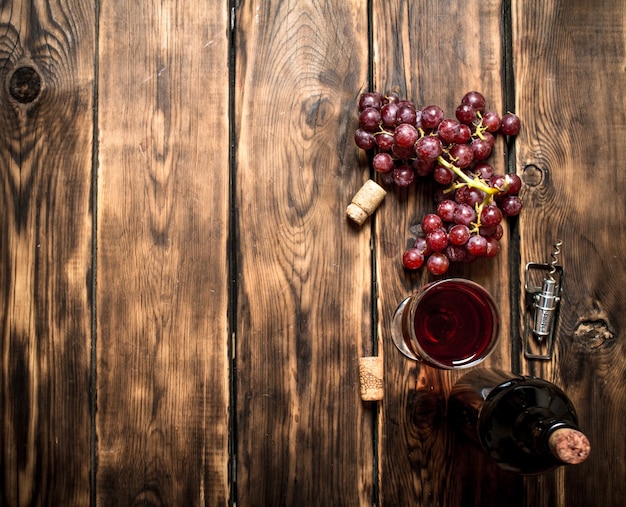 Vin rouge avec une branche de raisin et un tire-bouchon. Sur une table en bois.