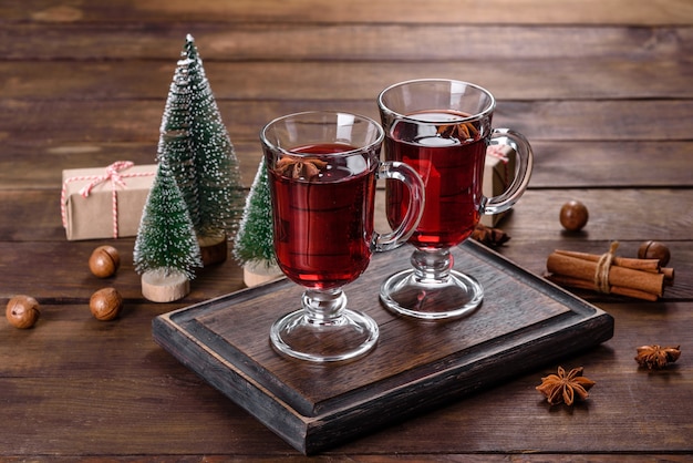 Vin rouge chaud de Noël aux épices et fruits sur une table sombre.