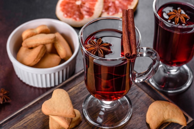 Vin rouge chaud de Noël aux épices et fruits sur une table sombre.